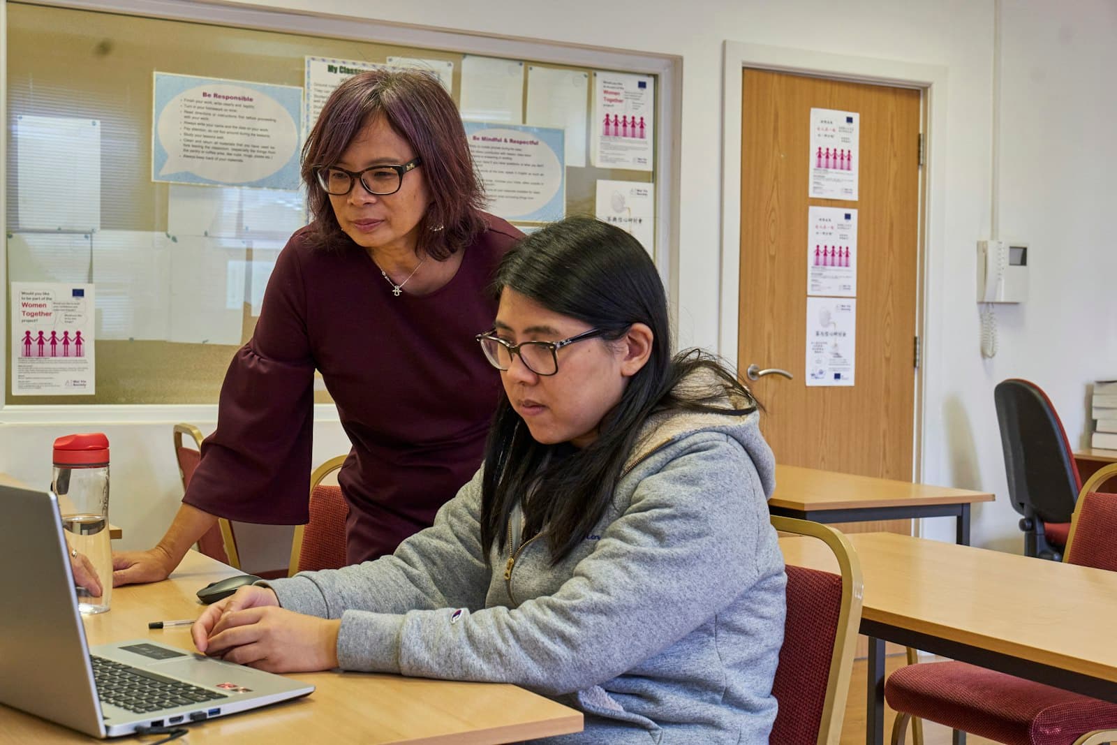A coach standing alongside an adult participant working at a laptop, the kind of patient one-to-one support our program will provide